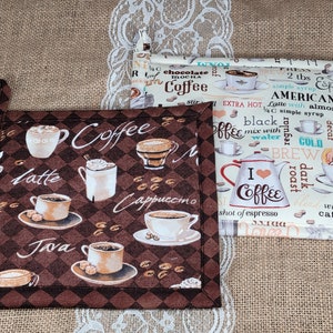 May include: Set of three brown and white cotton pot holders with a coffee theme. The pot holders feature various coffee drinks, including latte, cappuccino, and java. The text "Coffee" is printed on the pot holders.