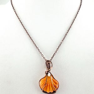 May include: A necklace featuring an orange seashell pendant wrapped in dark copper wire. A small white pearl is set at the top of the shell. The pendant hangs from a matching dark copper chain with a simple link design and a secure clasp.