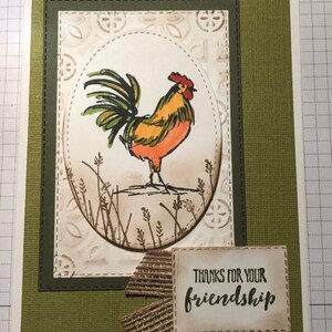 May include: Handmade greeting card with a rooster illustration in orange, yellow, and green. The card includes the text "THANKS FOR YOUR friendship" on a small rectangular label, with a burlap ribbon accent. The card has a green and white background.