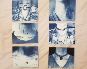 May include: A collection of cyanotype prints featuring different necklines and jewelry. The prints are on a light wood background.
