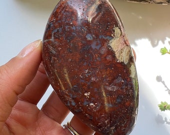 Può includere: Una pietra di diaspro rosso a forma di cuore liscia con macchie bianche e rosa. La pietra è lucidata e ha una forma naturale e organica.