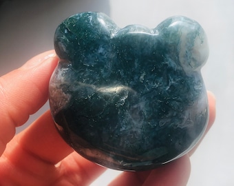 Puede incluir: Una piedra de ágata verde y blanca tallada en forma de oso. La piedra tiene un patrón de remolino y está pulida.