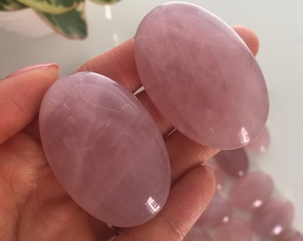 Può includere: Due pietre di quarzo rosa di forma ovale, una in ogni mano, con un mucchio di pietre di quarzo rosa più piccole sullo sfondo.