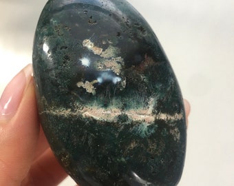 Könnte beinhalten: Ein glatter, ovaler grüner Moosachat-Handstein mit weißen und braunen Einschlüssen.