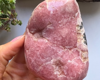 May include: A large, pink, heart-shaped crystal with white and black veins. The crystal is smooth and polished.