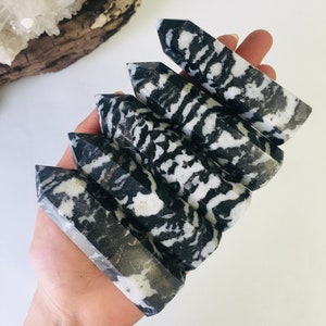 May include: Five black and white zebra jasper crystal points stacked on top of each other. The points are smooth and polished.