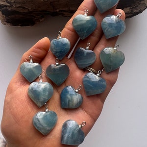 May include: A collection of twelve blue heart-shaped pendants made of polished agate. The pendants have a silver bail and are ready to be strung on a necklace or bracelet.