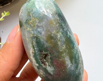 May include: A smooth, polished green, white and brown agate stone with a unique pattern. The stone is oval shaped and has a natural, organic look.