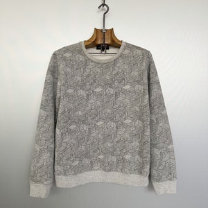 May include: A gray sweatshirt with a geometric pattern of interconnected cube-like shapes. The long-sleeved top has a crew neck and ribbed cuffs and hem. The design is a repeating pattern of gray lines on a lighter gray background.