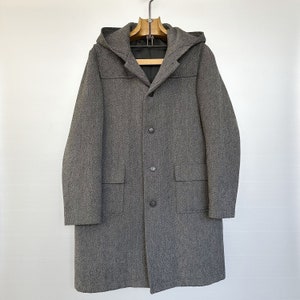 Peut inclure: Un manteau gris à capuche avec fermeture boutonnée et deux poches. Le manteau est à motif chevron.