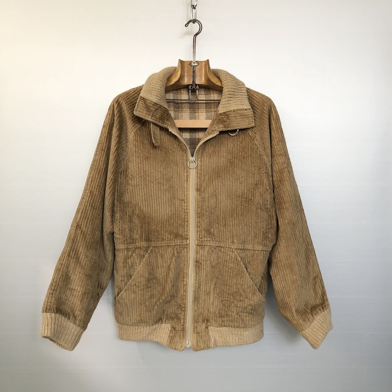 May include: A brown corduroy jacket with a zipper closure and a plaid lining. The jacket has a ribbed knit collar, cuffs, and hem.