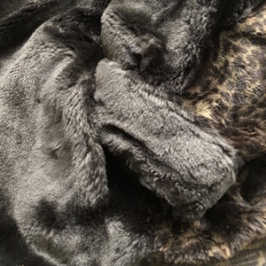 May include: Close-up of a black faux fur fabric with a brown and black patterned faux fur fabric underneath.