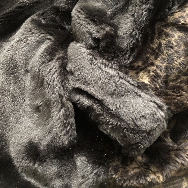 May include: Close-up of a black faux fur fabric with a brown and black patterned faux fur fabric underneath.