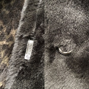 May include: Close-up of a black faux fur coat with a silver metal tag that reads "DASCO".