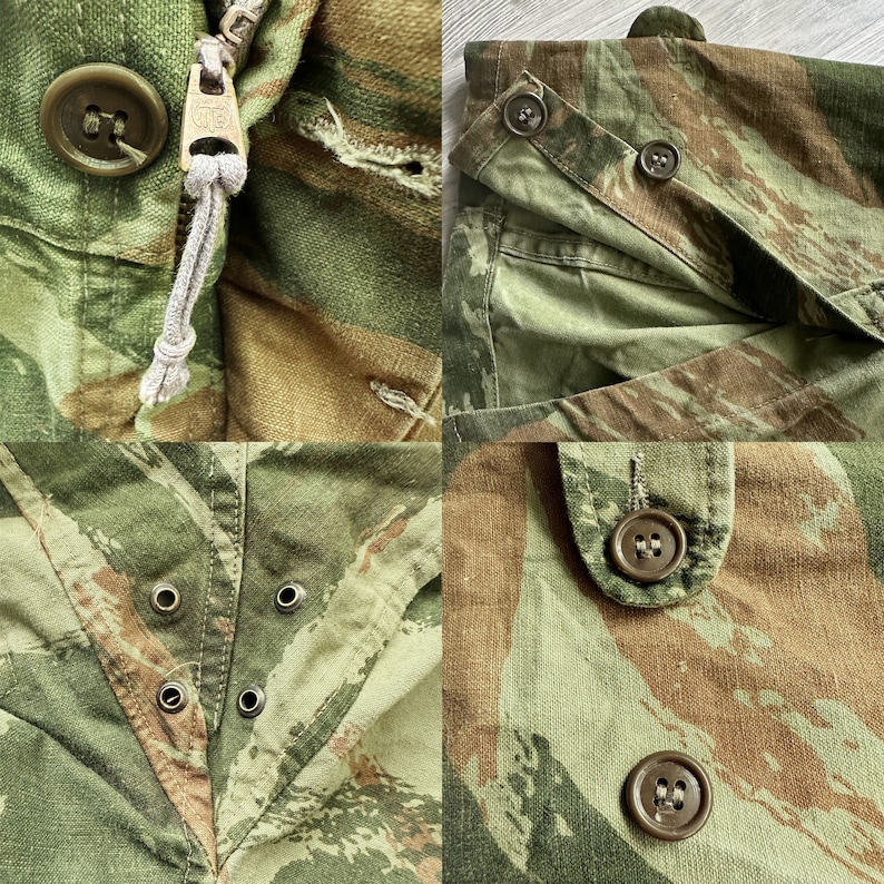 May include: Close-up of a camouflage fabric with multiple buttons and a zipper. The fabric is a mix of green, brown, and tan.