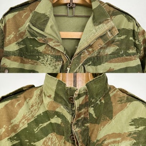 May include: A camouflage jacket with a button-up front and a zipper closure. The jacket has a green, brown, and tan camouflage pattern.