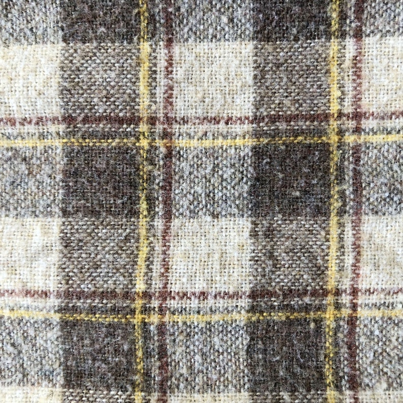 May include: A close-up of a brown and white plaid fabric with a yellow and red woven pattern.