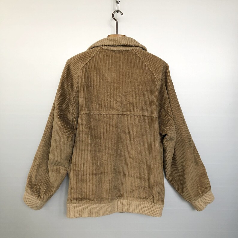 May include: A brown corduroy jacket with a beige collar and cuffs. The jacket has a zipper closure and two pockets.