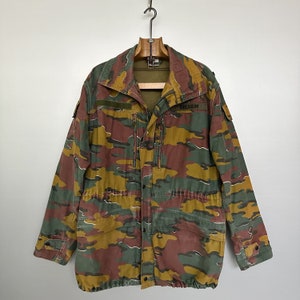 Könnte beinhalten: Eine Tarnjacke mit Reißverschluss und Knöpfen. Die Jacke hat einen Aufnäher mit der Aufschrift "BELGIEN" am linken Ärmel.