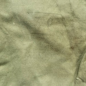 May include: A close-up of a green canvas fabric with a textured weave. The fabric has a few dark brown stains.