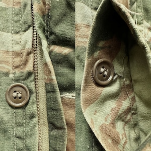 May include: Close-up of a green, brown, and tan camouflage fabric with a zipper and two brown buttons. The fabric is textured and has a worn look.
