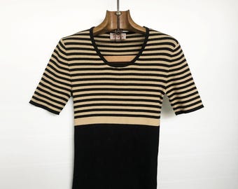 May include: A short-sleeved, ribbed knit top in black and tan horizontal stripes. The top transitions to solid black below the bust line. The scoop neck top is hanging on a wooden hanger against a white background.
