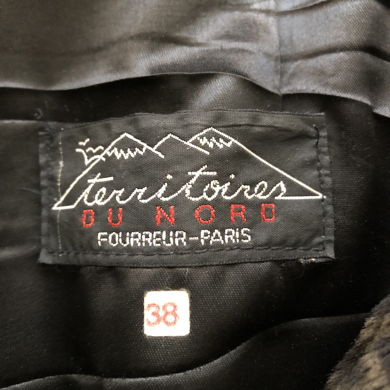 May include: A black label with white text that reads "Territoires Du Nord Fourreur-Paris" and a mountain range graphic. The label has a red size tag that reads "38".