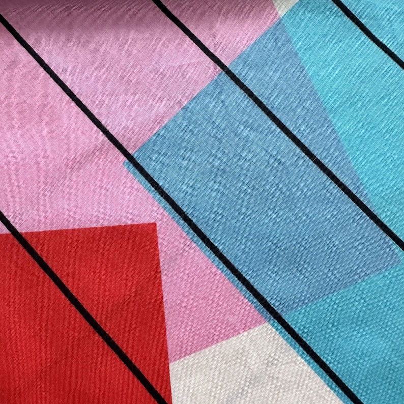May include: Abstract textile pattern with geometric shapes in pink, red, blue, and white, and black diagonal lines. The fabric has a textured appearance, possibly woven or printed. The colour scheme is vibrant and modern.