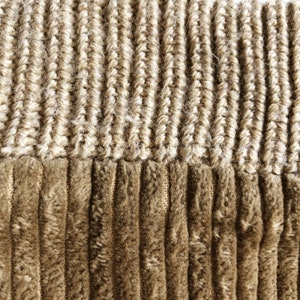 May include: Close-up of a brown corduroy fabric with a beige knit trim. The fabric has a textured, ribbed appearance.