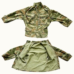 May include: A green and brown camouflage jacket with a zipper closure and multiple pockets. The jacket is shown both closed and open to reveal the lining.
