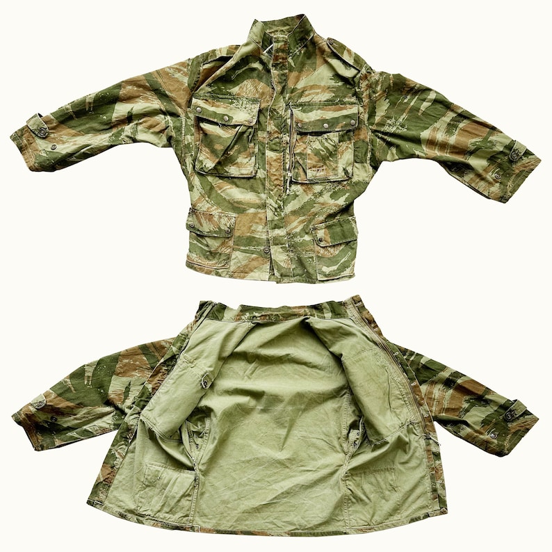 May include: A green and brown camouflage jacket with a zipper closure and multiple pockets. The jacket is shown both closed and open to reveal the lining.