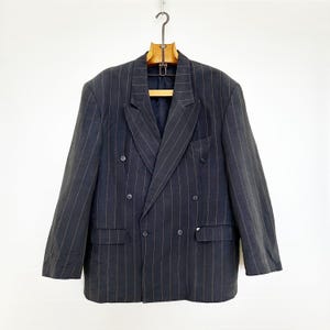 May include: A dark blue double-breasted blazer with thin vertical stripes. The blazer has four buttons and two flap pockets.