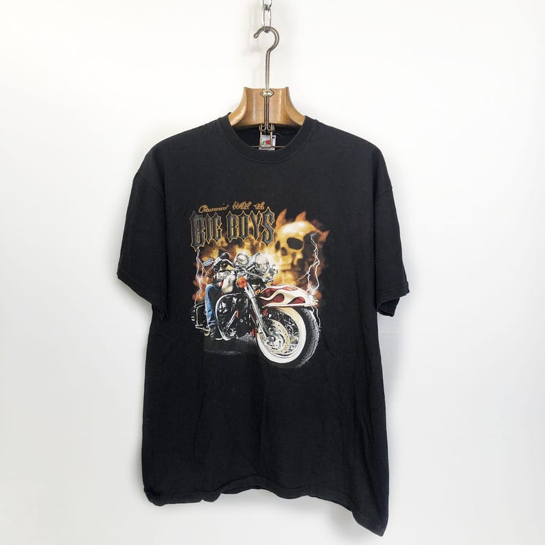K&ouml;nnte beinhalten: Schwarzes T-Shirt mit einem Motiv eines Motorradfahrers mit einem Totenkopf und Flammen. Der Text "Cruisin' hell on Big Boys" ist auf dem Shirt aufgedruckt.