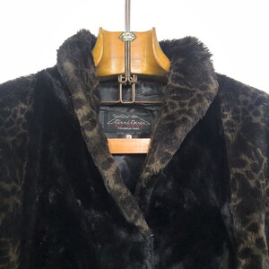 May include: A black faux fur coat with a leopard print pattern. The coat has a large collar and a label that reads "Territoires Du Nord Fourrurier Paris".