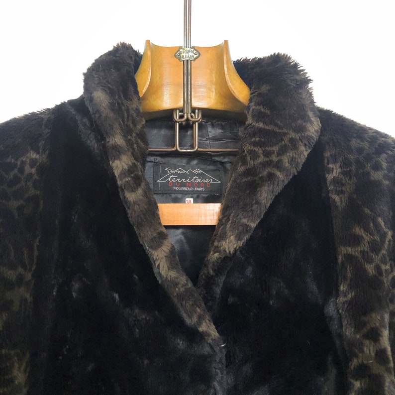 May include: A black faux fur coat with a leopard print pattern. The coat has a large collar and a label that reads "Territoires Du Nord Fourrurier Paris".