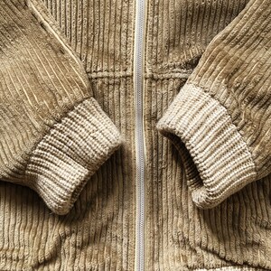 May include: A brown corduroy jacket with a zipper closure and ribbed cuffs. The jacket is made of a soft, textured fabric.