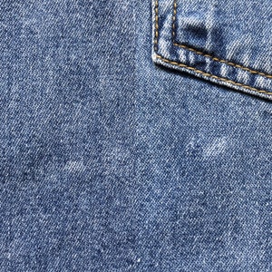 Pode incluir: Close-up de tecido denim azul com um canto de bolso. O denim tem uma apar&ecirc;ncia texturizada com detalhes de tecido vis&iacute;veis. O canto do bolso &eacute; refor&ccedil;ado com costuras amarelas, adicionando um elemento de contraste.