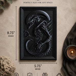 May include: Black framed relief sculpture of an Alien creature, 8.75 inches high and 5.75 inches wide. The artwork is a detailed depiction of the creature's form. The text "DIMENSIONS" and "PERFECT SIZE FOR ANY SPACE" are visible.