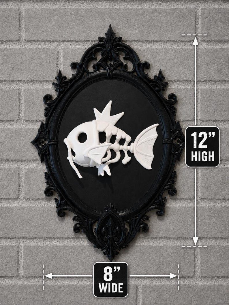 May include: A white fish skeleton relief mounted on a black oval background within an ornate black frame. The piece measures 12 inches high and 8 inches wide, featuring a stylized skeletal fish design with a crown-like fin on its head.