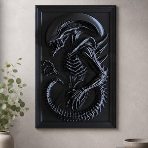 May include: A black framed relief sculpture of an Alien creature. The artwork features a detailed depiction of the extraterrestrial's skeletal structure, elongated head, and segmented tail. The relief is mounted in a black frame, creating a striking contrast against the wall.