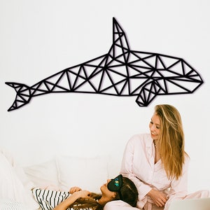 Op de afbeelding: Twee mensen ontspannen in een slaapkamer met een geometrische zwarte walvis wanddecoratie. Een persoon ligt met een slaapmasker op, terwijl de ander zit met een laptop.