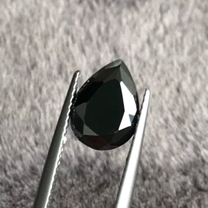 May include: A black pear-shaped gemstone held by tweezers.