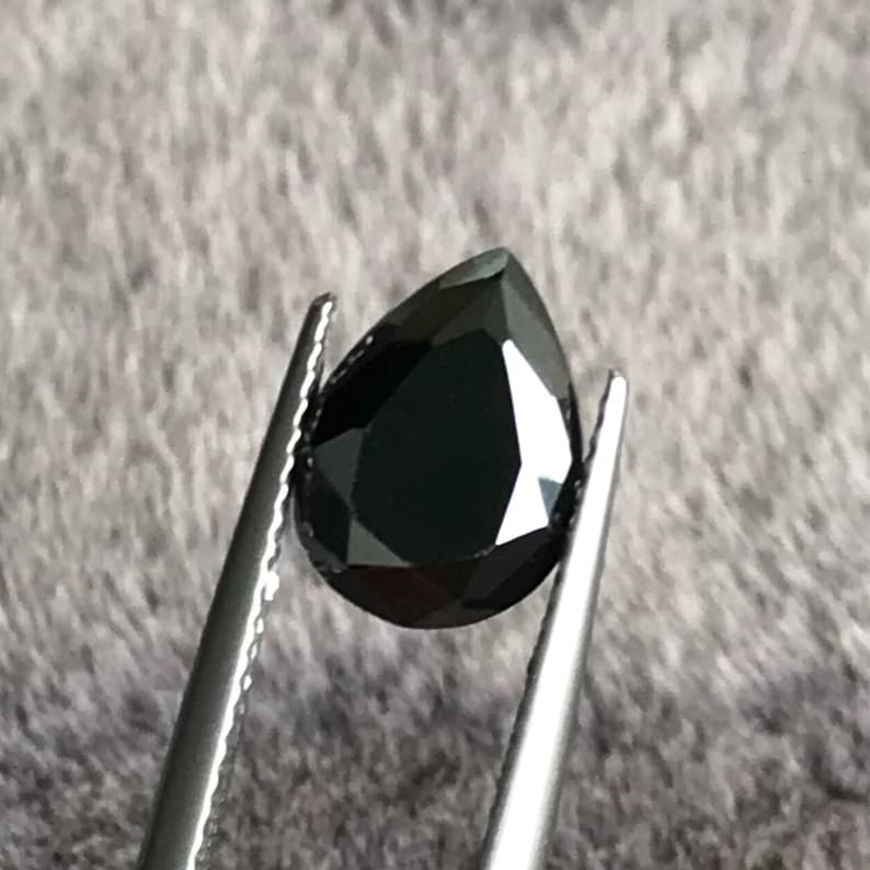 May include: A black pear-shaped gemstone held by tweezers.