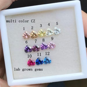 May include: A white box with a variety of heart-shaped lab-grown gems in different colors. The gems are labeled with numbers 1 through 12. The text "multi color CZ" and "lab grown gems" is printed on the box.