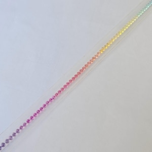 Könnte beinhalten: Ein zartes, schmales Armband mit einem Farbverlauf aus kleinen, runden Perlen. Die Farben wechseln von Lila zu Rosa, dann zu Orange, Gelb und schließlich zu einem hellen Grün. Das Armband liegt auf weißem Hintergrund.