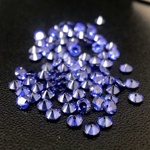 May include: A large group of blue sapphire gemstones, scattered on a black surface. The gemstones are faceted and have a brilliant shine.