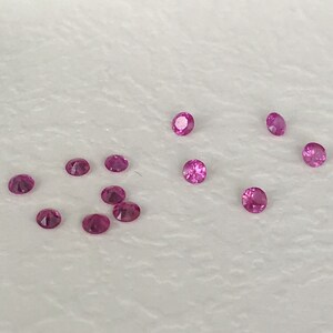 Puede incluir: Una colección de gemas rosadas, esparcidas sobre una superficie blanca. Las gemas son redondas y tienen un acabado brillante.