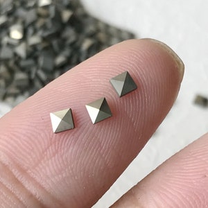Op de afbeelding: Drie zilveren piramidevormige strasssteentjes op een vinger.