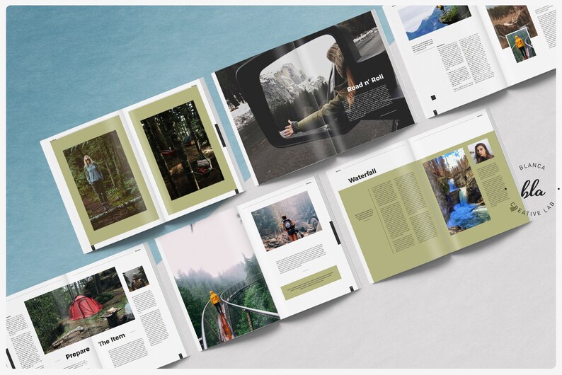 May include: A spread of open magazines with nature photography and text. One spread features a person in a car with the text "Road n' Roll". Other spreads show forest scenes, a waterfall, and a red tent. The magazines are on a light blue surface.