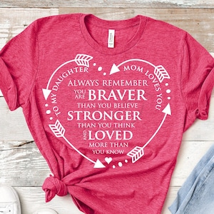 May include: A pink t-shirt with a white heart design that says "To my daughter, always remember you are braver than you believe, stronger than you think, and loved more than you know. Mom loves you."